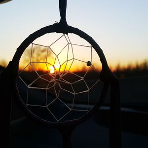 Close-up of dreamcatcher against sun and sky