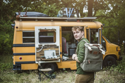 Rear view portrait of man with backpack walking towards motor home in forest during camping
