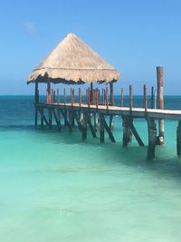 Thatched roof on pier over sea against blue sky