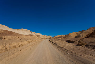 Road amidst desert against clear blue sky