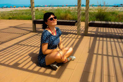 Smiling young woman wearing sunglasses while sitting on tiled floor