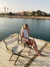 Woman sitting on chair by lake