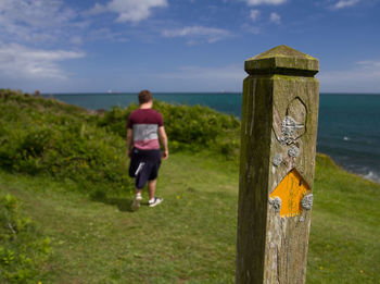 Rear view full length of boy by wooden post against sea