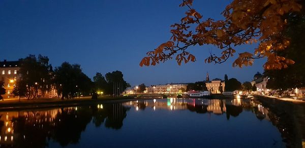 Illuminated buildings by lake against sky at night