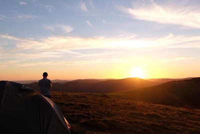 Rear view of man standing on mountain against sky at sunset