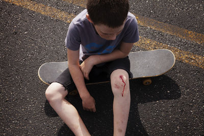 High angle view of boy with wounded knee sitting on skateboard