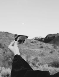 Cropped hand holding broken mirror against sky