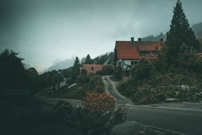 Road amidst trees and buildings against sky