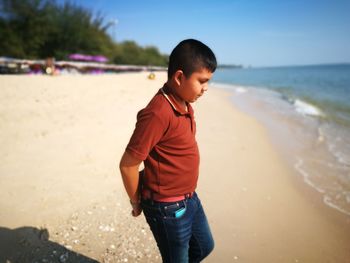 Boy standing on beach against sky