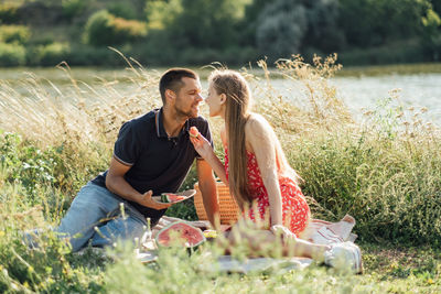 Young couple in love on summer picnic with watermelon. loving couple sitting by the river, talking