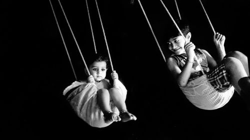 Siblings in swing against black background