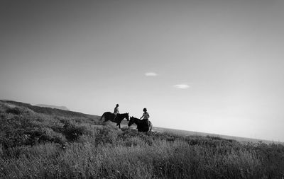 People riding horses on field against sky