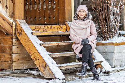Warmly dressed young woman posing on the porch of a wooden house in the village. winter 