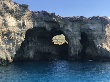 Rock formations by sea against clear blue sky