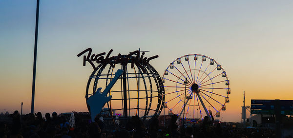 Silhouette people at amusement park against sky during sunset