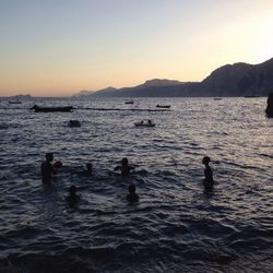 Silhouette people swimming in sea against clear sky