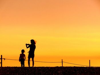 Silhouette mother and daughter standing against orange sky