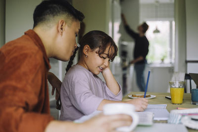 Smiling girl doing homework while sitting with gay father at table in home