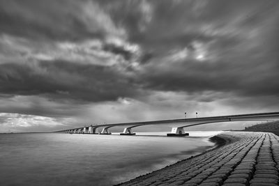 Bridge over calm sea against cloudy sky