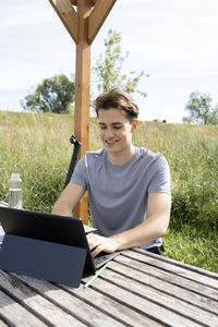 Portrait of young man using digital tablet while sitting on field