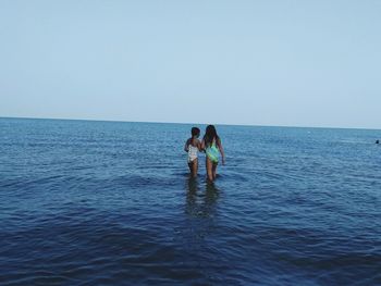 Women standing in sea against clear sky