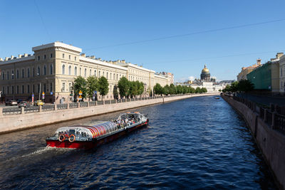 View of buildings by river against clear blue sky