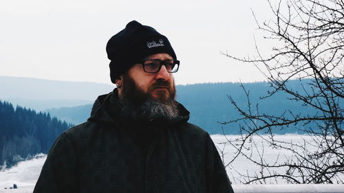 Man looking away while standing against sky during winter