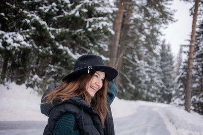 Smiling woman wearing hat standing against snow covered trees