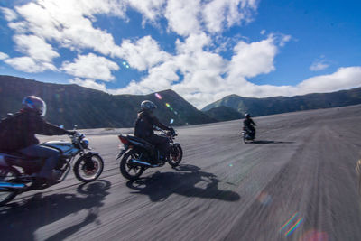 Men riding motorcycles on road against sky