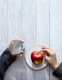 Minimal healthy snack concept. the child's hands are holding an apple and a glass of water. 