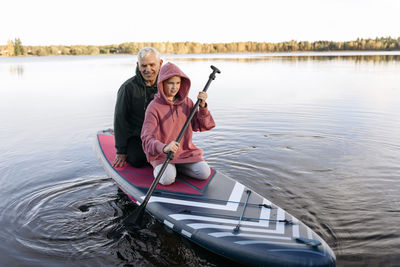 Grandfather looking at girl paddleboarding in lake