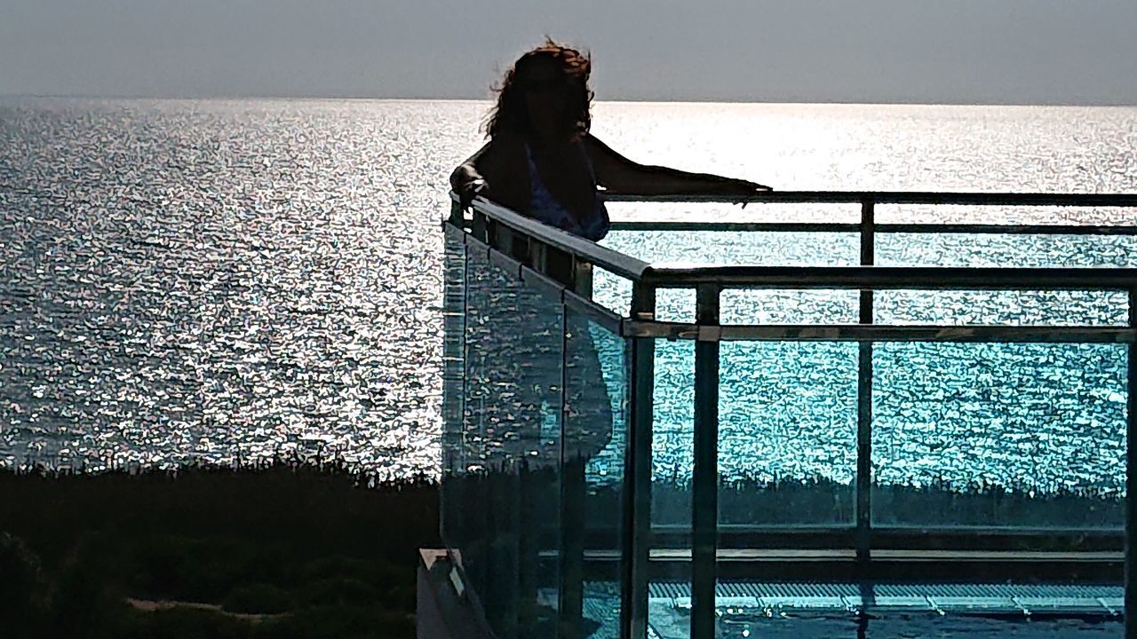 WOMAN STANDING IN SWIMMING POOL AGAINST SEA