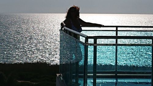 Woman standing by swimming pool against sea