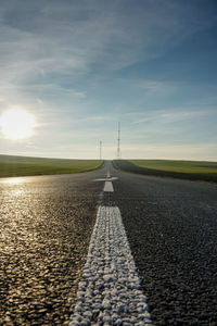 Surface level of road amidst field against sky