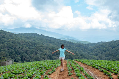 Full length of woman with arms outstretched standing on agricultural field against sky