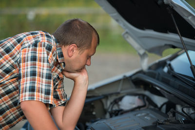 Side view of man examining car engine on road