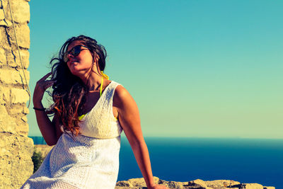 Beautiful young woman standing in sea against clear sky