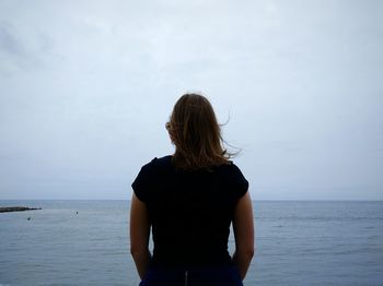 Rear view of woman standing in front of sea against sky