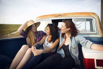 Cheerful friends sitting side by while traveling side in pick-up truck