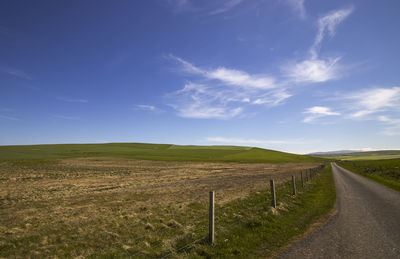 Empty road amidst field against sky