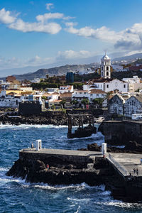 Buildings by sea against blue sky