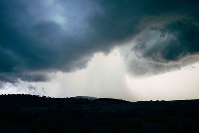 Low angle view of storm clouds over silhouette landscape