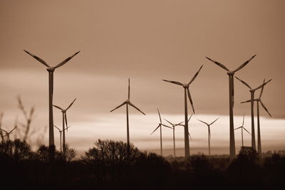 Silhouette wind turbines on field against sky during sunset