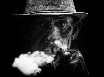 Close-up portrait of person wearing hat against black background