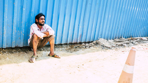 Portrait of young man sitting on beach against blue wall