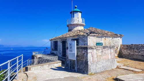 Lighthouse by sea against clear blue sky