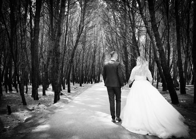 Rear view of wedding couple walking on road amidst trees