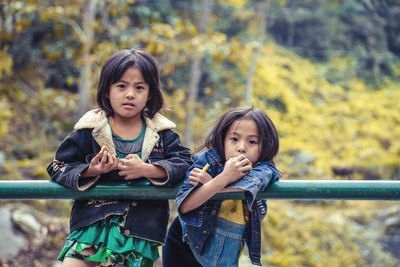 Portrait of siblings standing by railing against trees