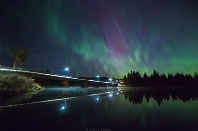 Illuminated bridge over lake against sky at night