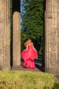 Full length of young woman in pink evening gown dancing at colonnade